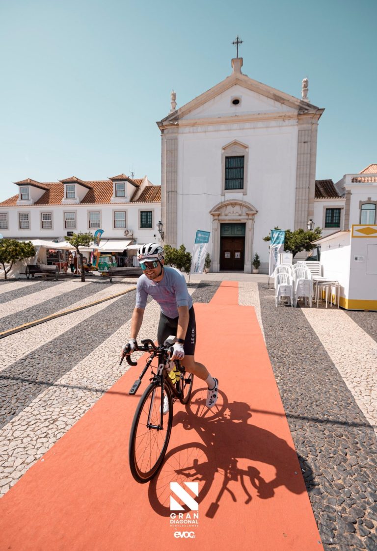 Radfahrer auf rotem Teppich vor einer historischen Kirche mit Markisen.