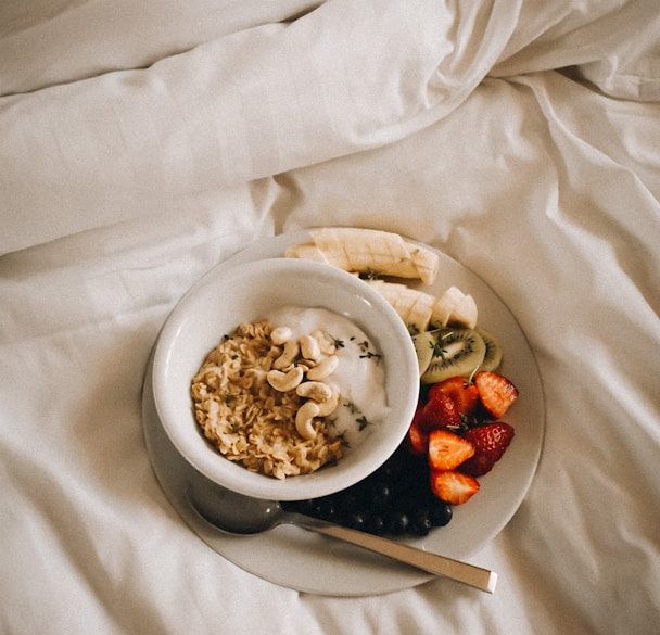 Schüssel Haferbrei mit Joghurt, Bananen, Erdbeeren und Trauben auf einem Bett.