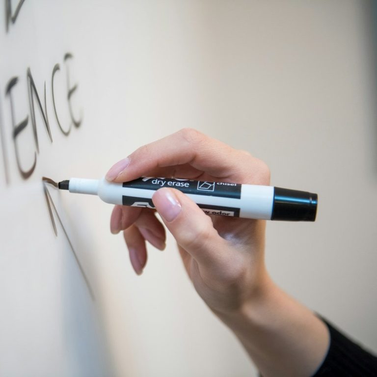 Eine Hand hält einen schwarzen Marker, während sie ein Wort an eine Wand schreibt.