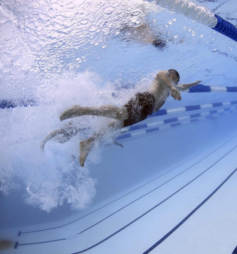 Ein Schwimmer taucht ins Wasser und zieht durch die Bahn in einem Schwimmbecken.