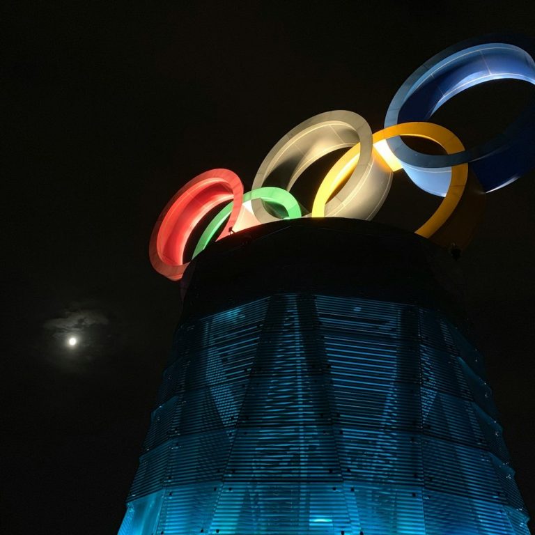 Olympische Ringe leuchten in der Nacht über einem beleuchteten Turm.