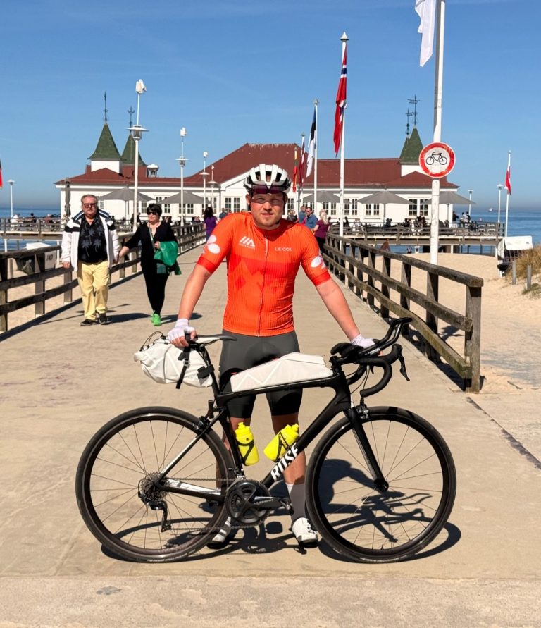 Der Gründer Tom Hornuff mit seinem Rennrad vor einer Seebrücke am Meer