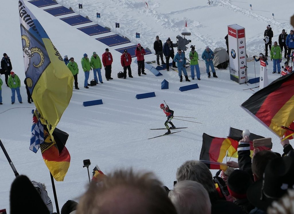Biathlet bei einem Wettkampf, umgeben von jubelnden Zuschauern und Fahnen.